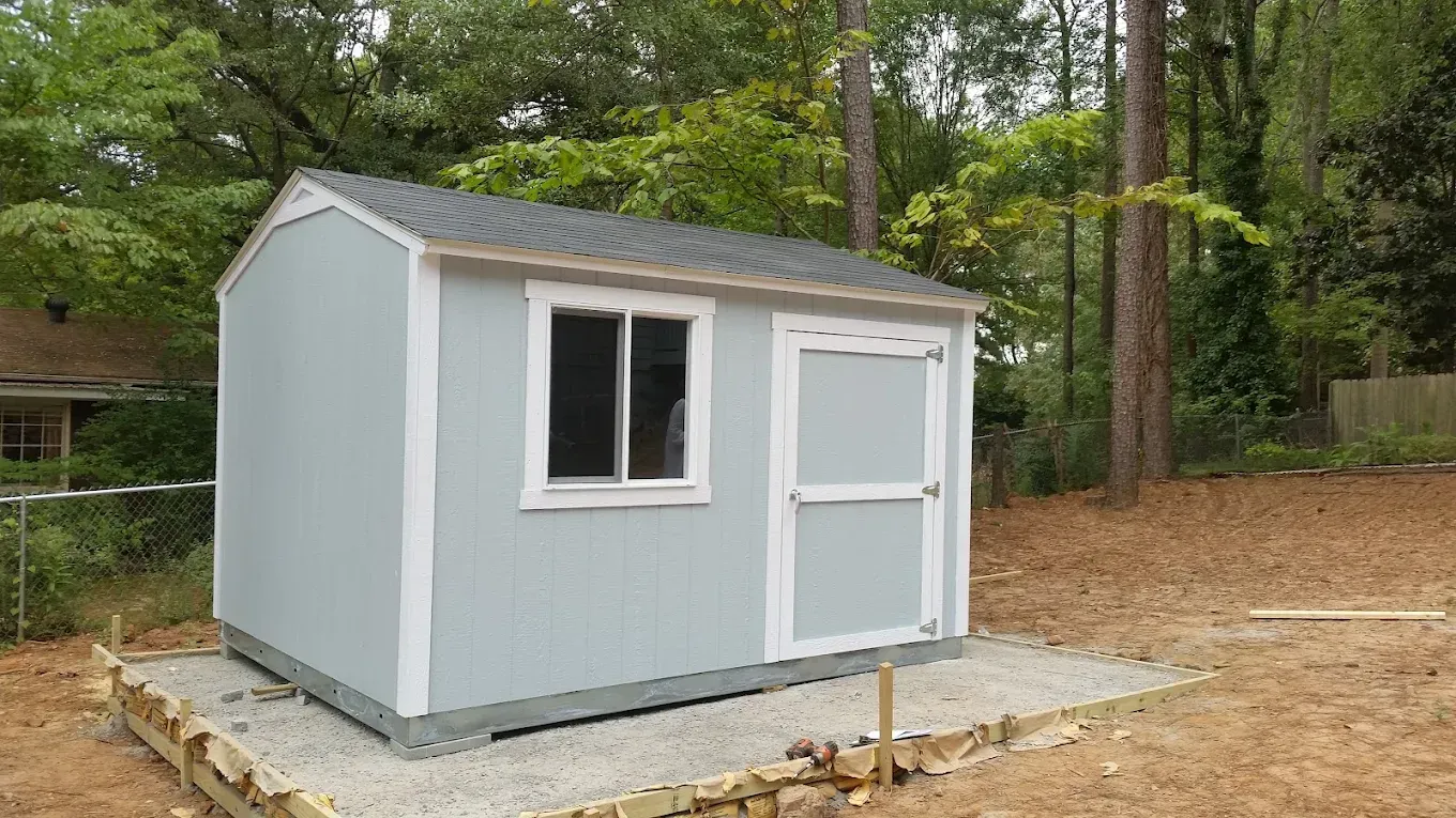 A small shed is sitting on top of a pile of gravel in a yard.