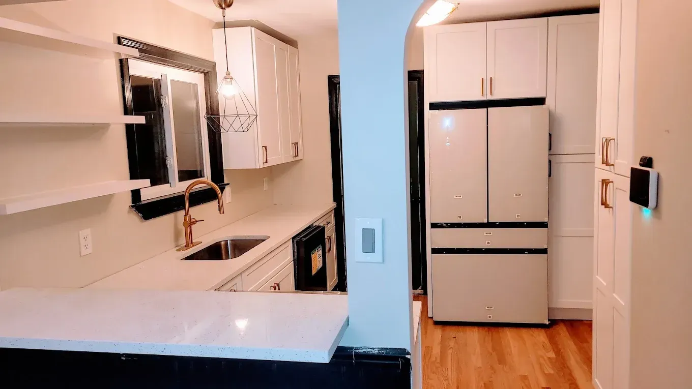 A kitchen with white cabinets , a refrigerator , a sink , and a window.