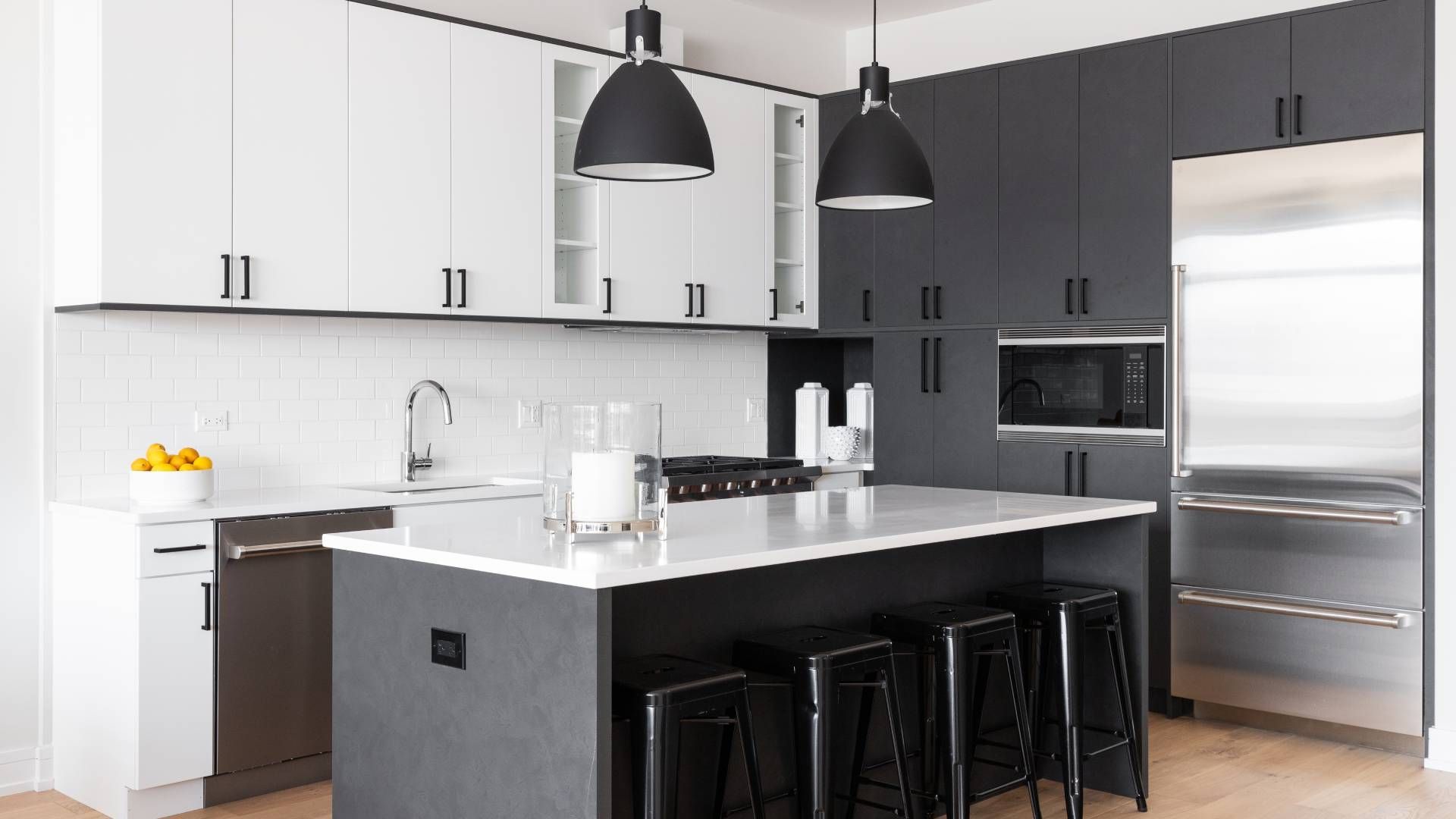 A kitchen with black and white cabinets , stainless steel appliances , and a large island.