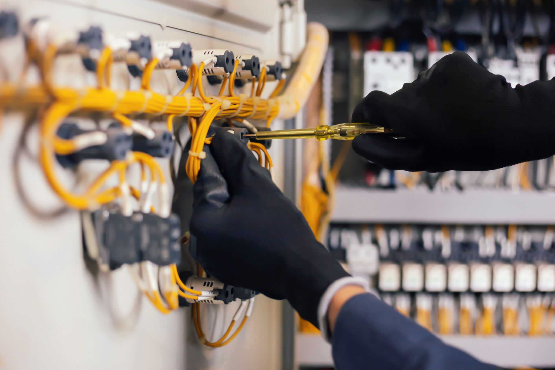 Gloved hands wiring a circuit panel with yellow cables and electrical components