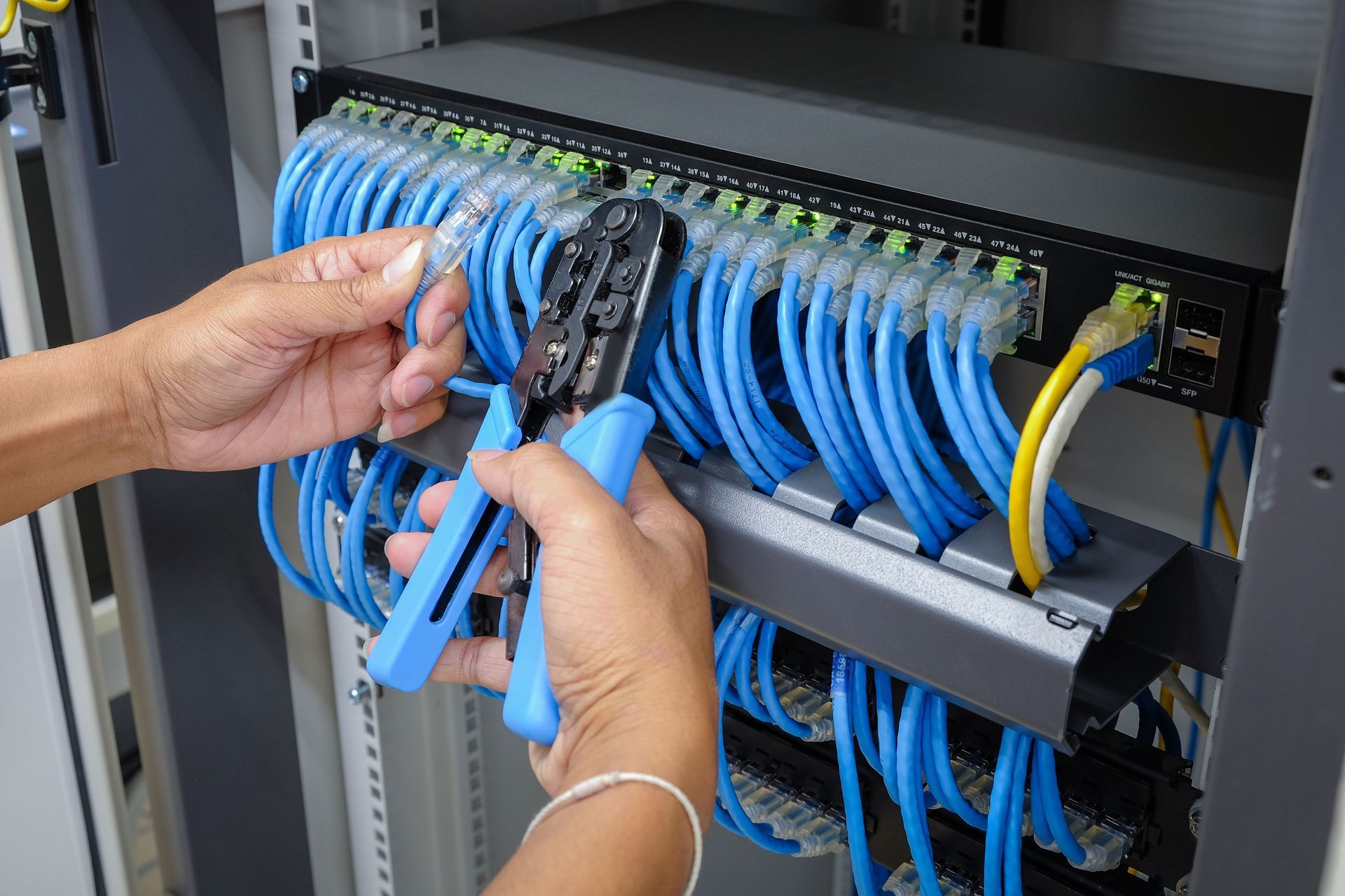 Hands connecting blue Ethernet cables in a network server rack