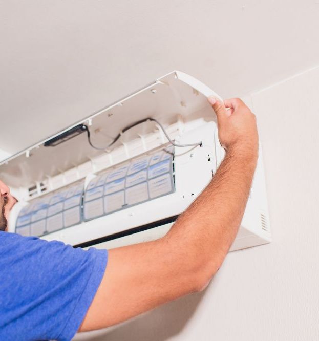 A Man is Fixing an Air Conditioner on the Wall — Anderson Electrical & Air in Taree, NSW