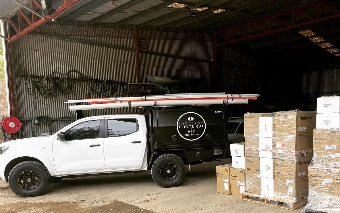 A white truck is parked in front of a warehouse filled with boxes — Anderson Electrical & Air in Taree, NSW