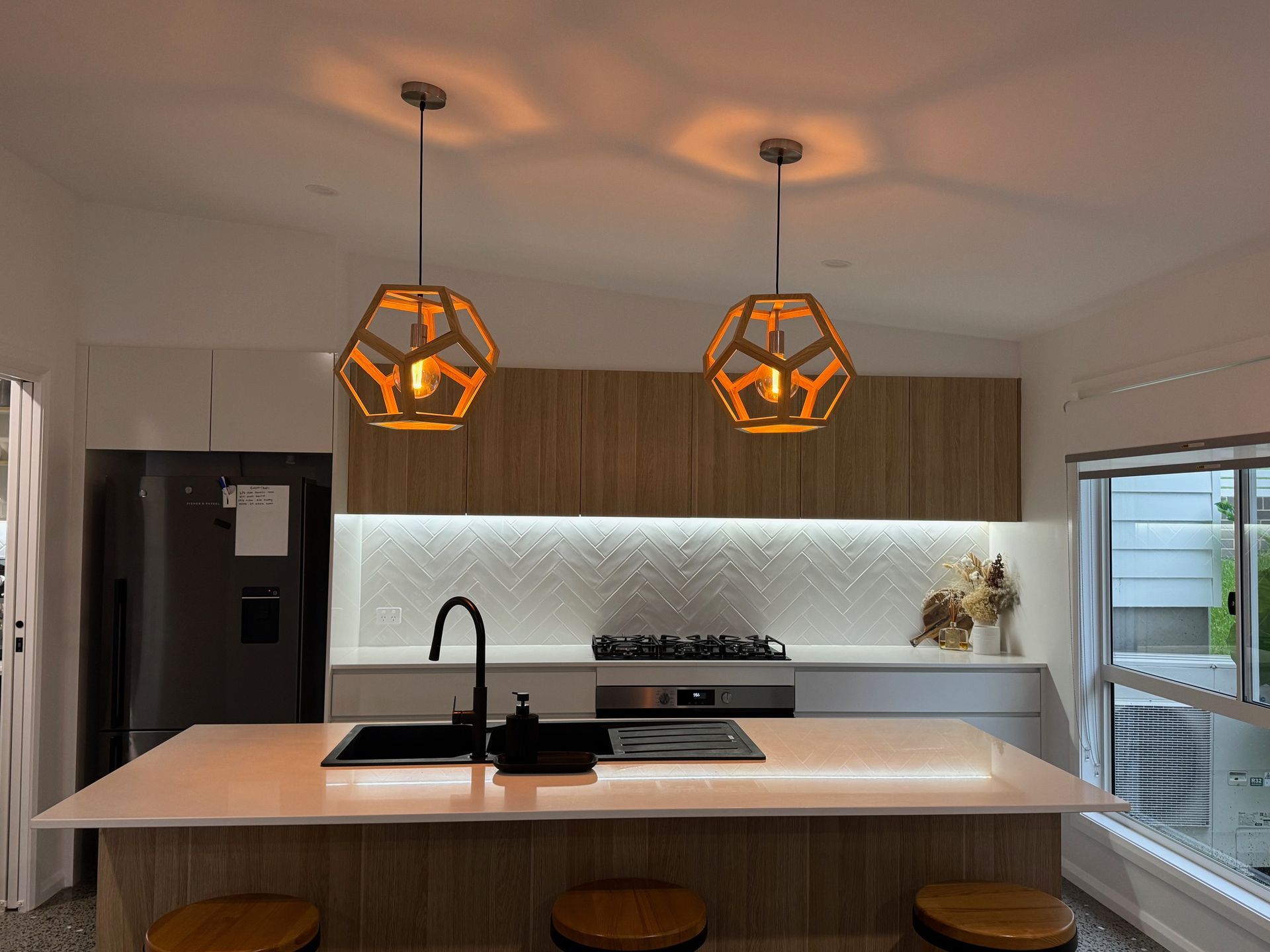 A kitchen with a sink , stove , refrigerator and two pendant lights hanging from the ceiling — Anderson Electrical & Air in Taree, NSW