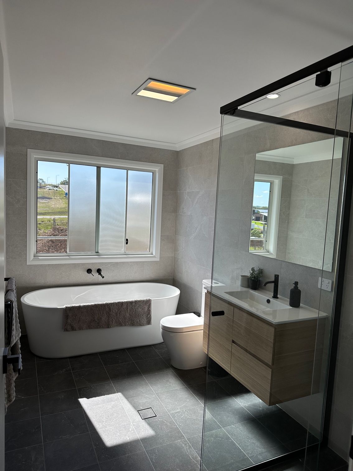 A bathroom with a tub , toilet , sink and mirror — Anderson Electrical & Air in Taree, NSW