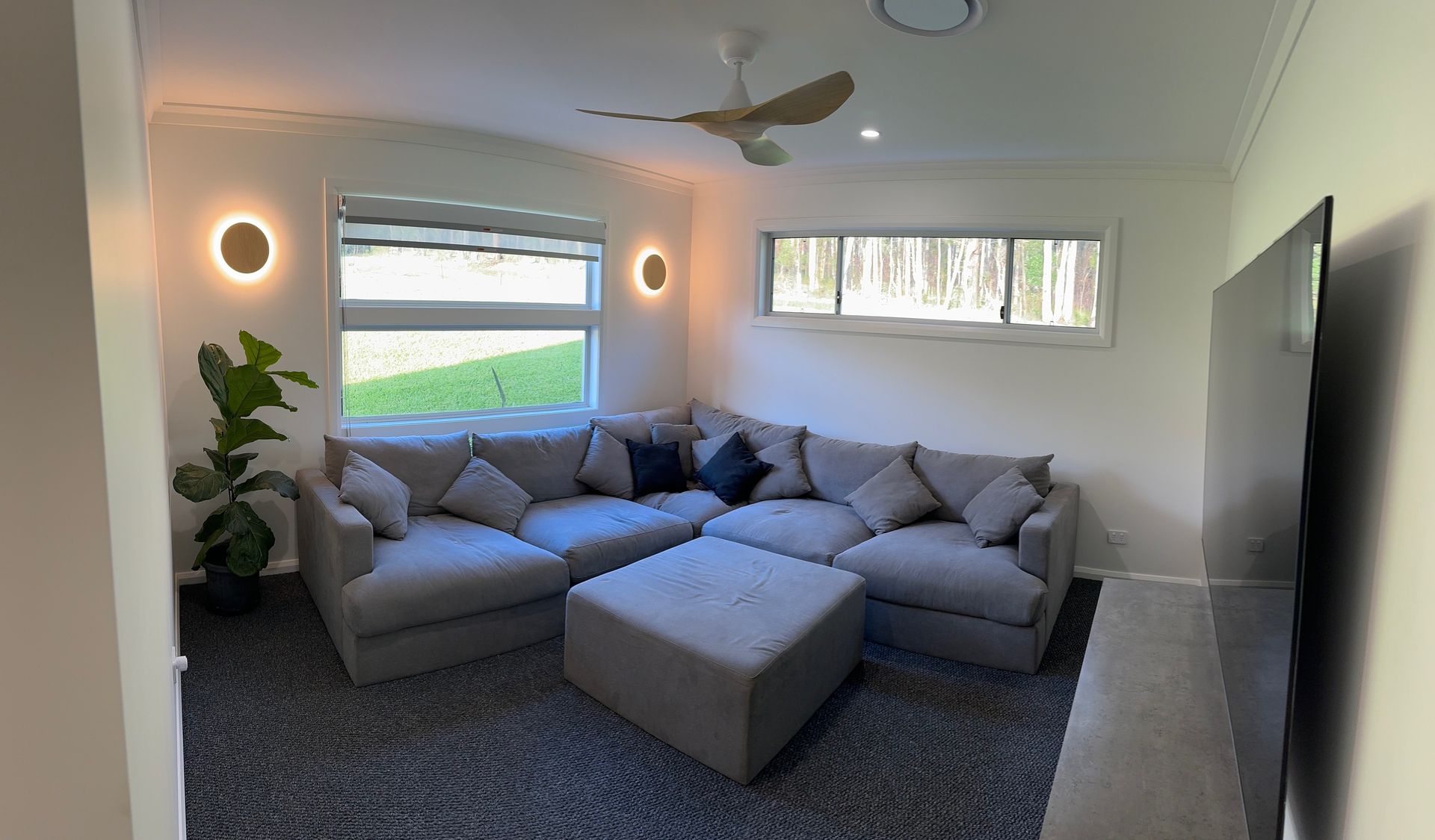 A living room with a large sectional couch and ottoman — Anderson Electrical & Air in Tuncurry, NSW