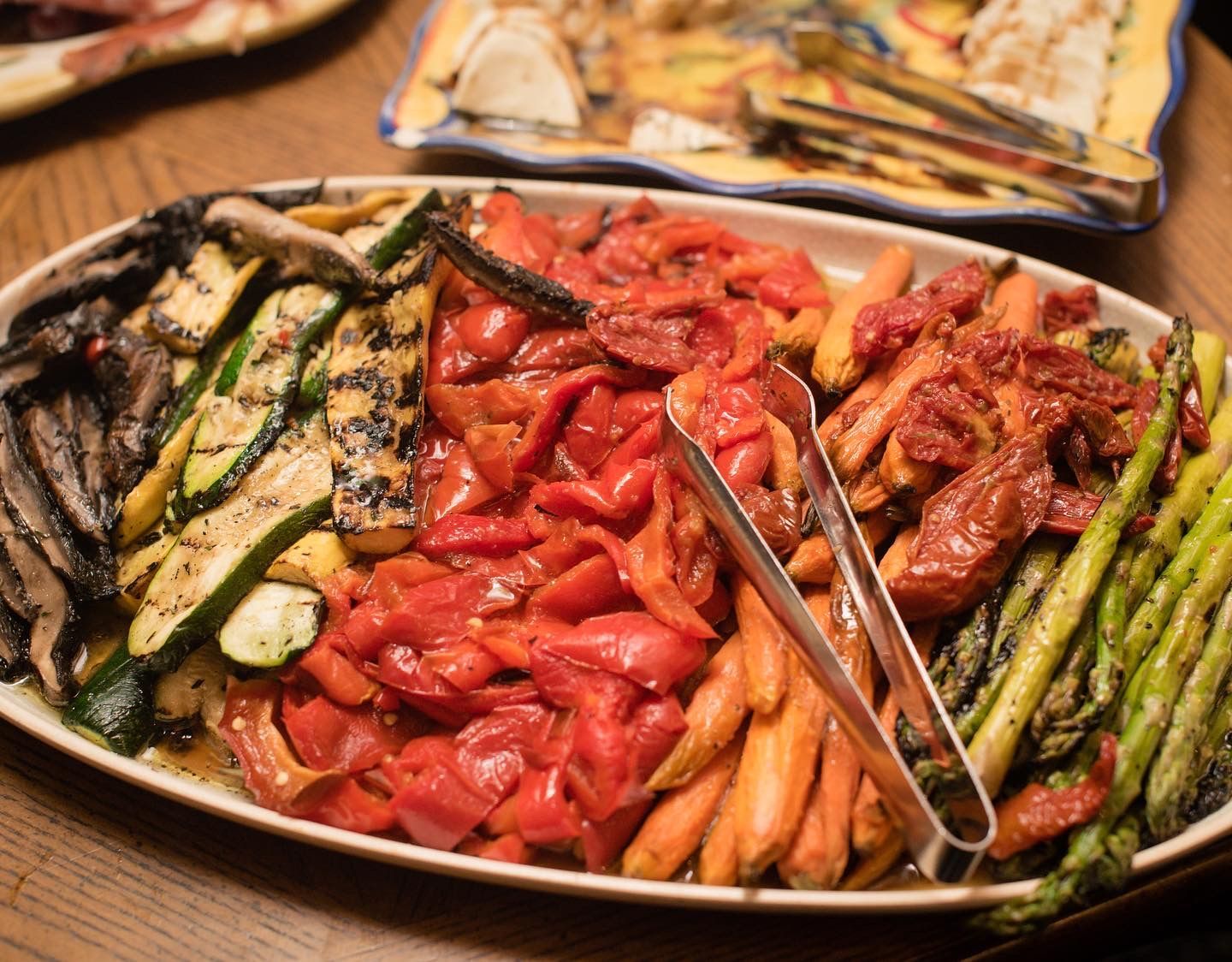 A plate of vegetables with tongs on a table.