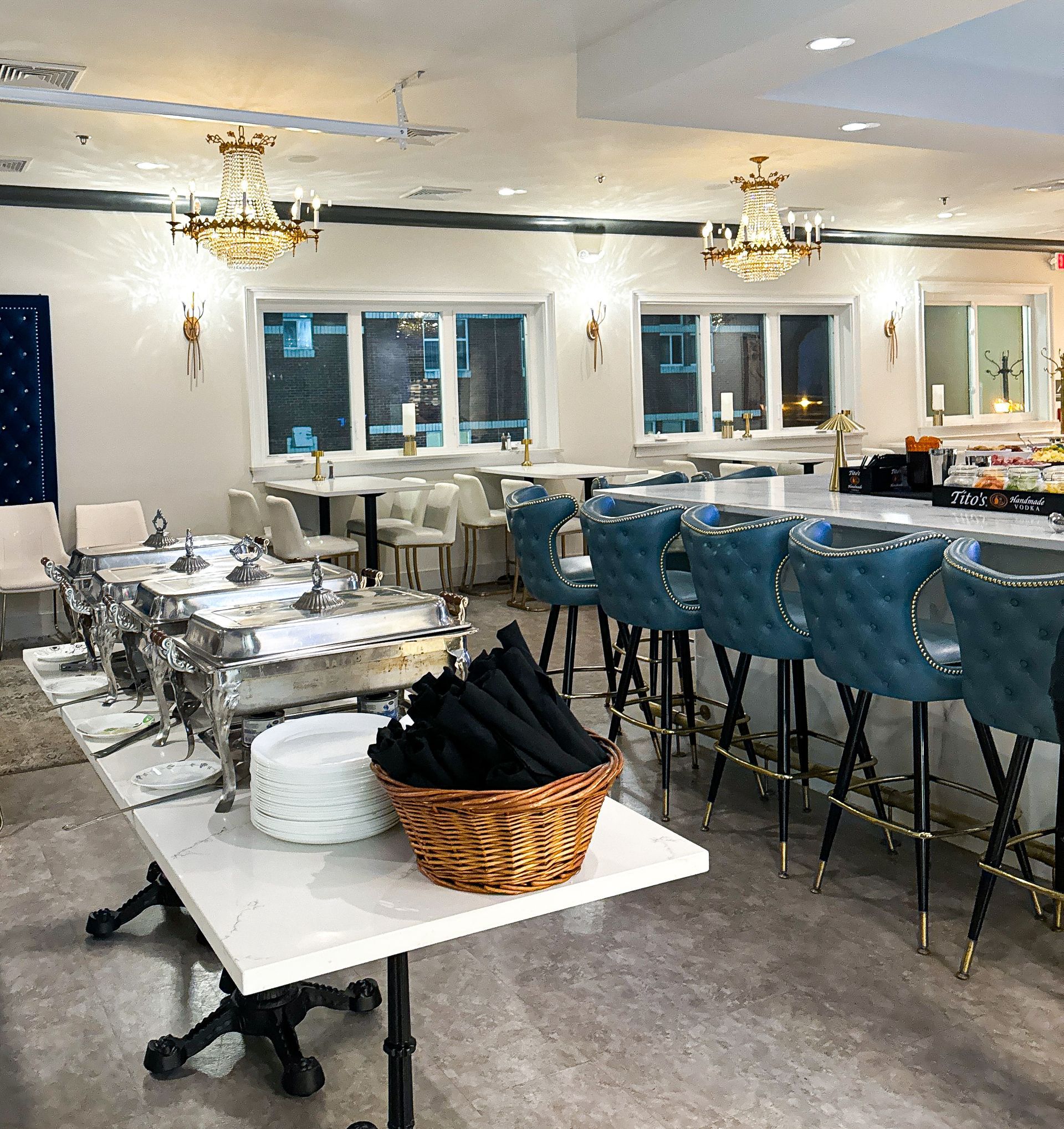 A large room with tables and chairs and a buffet table with a basket of napkins on it.