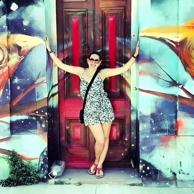 A happy woman posing in the middle of a colorful bird mural on a wall during the walk through Valparaiso with ChileVive Tours.