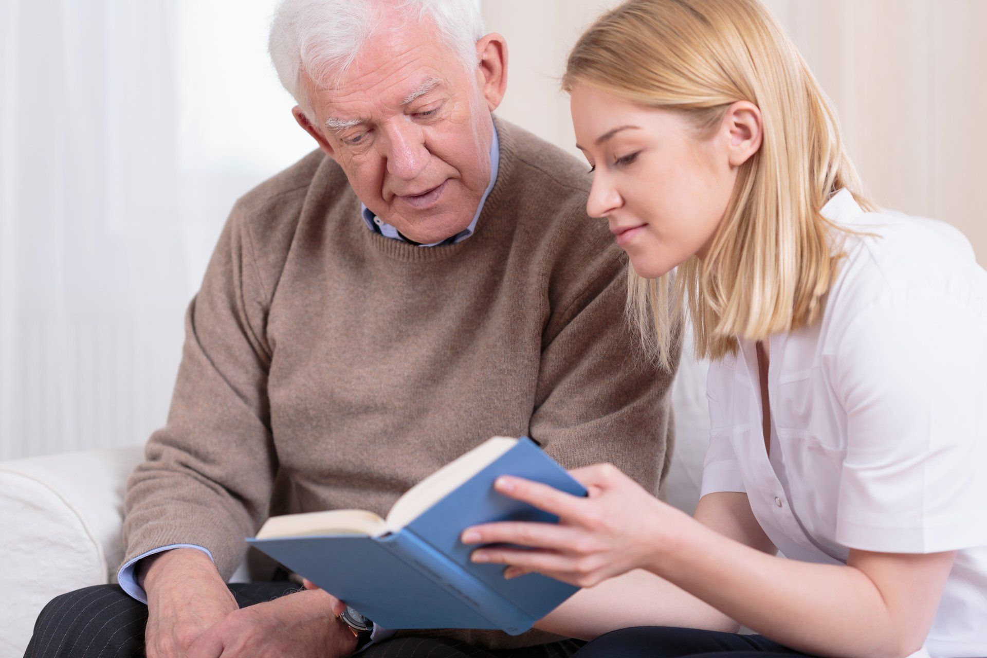 Enfermera leyendo libro a un adulto anciano