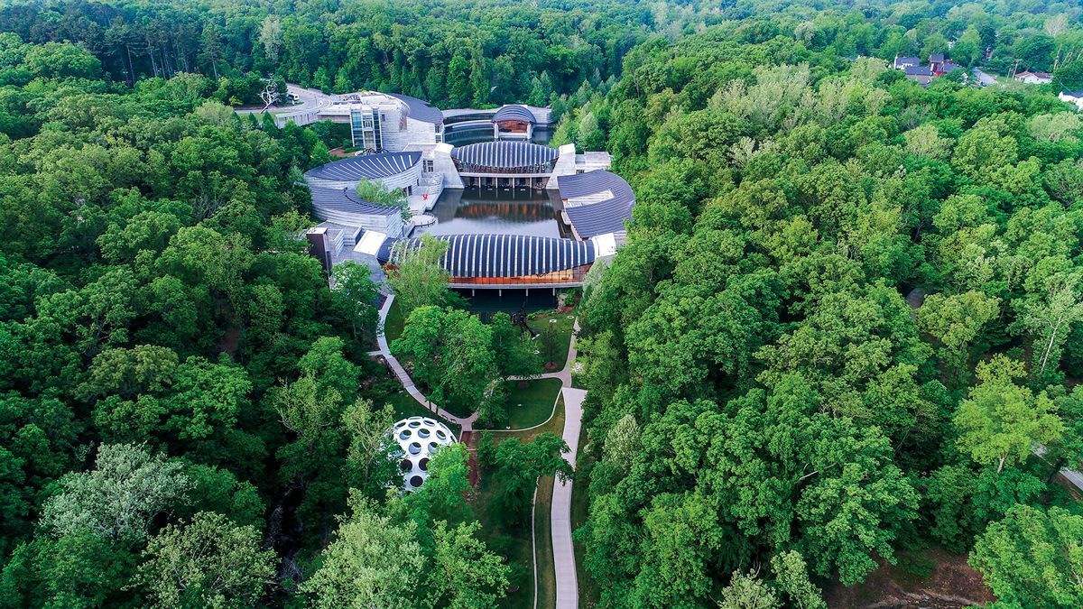 Aerial view of a large building complex surrounded by dense green forest and a winding road