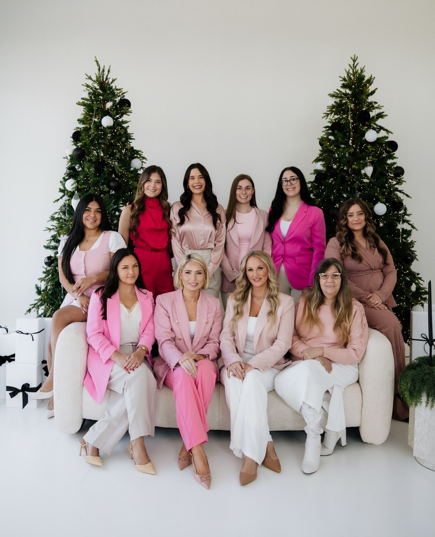 Group posed in pink and white outfits before decorated Christmas trees.