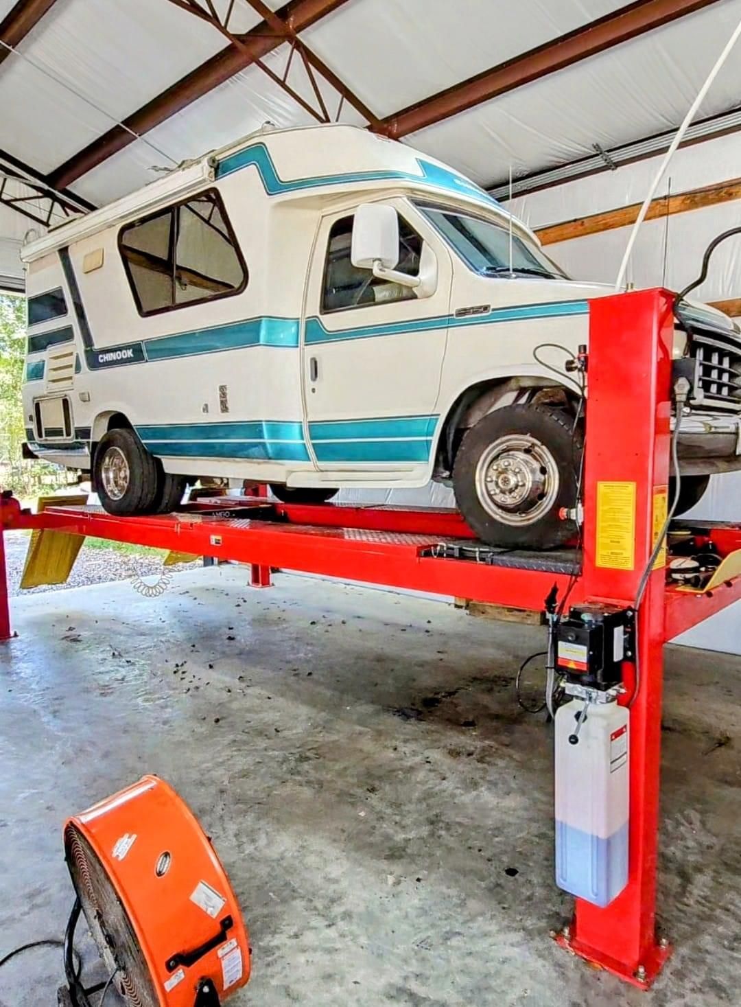 A camper van is sitting on top of a red lift in a garage.