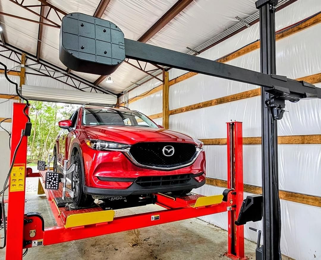 A red car is sitting on a lift in a garage.