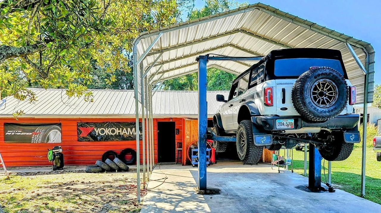 A jeep is sitting on a lift in front of a garage.