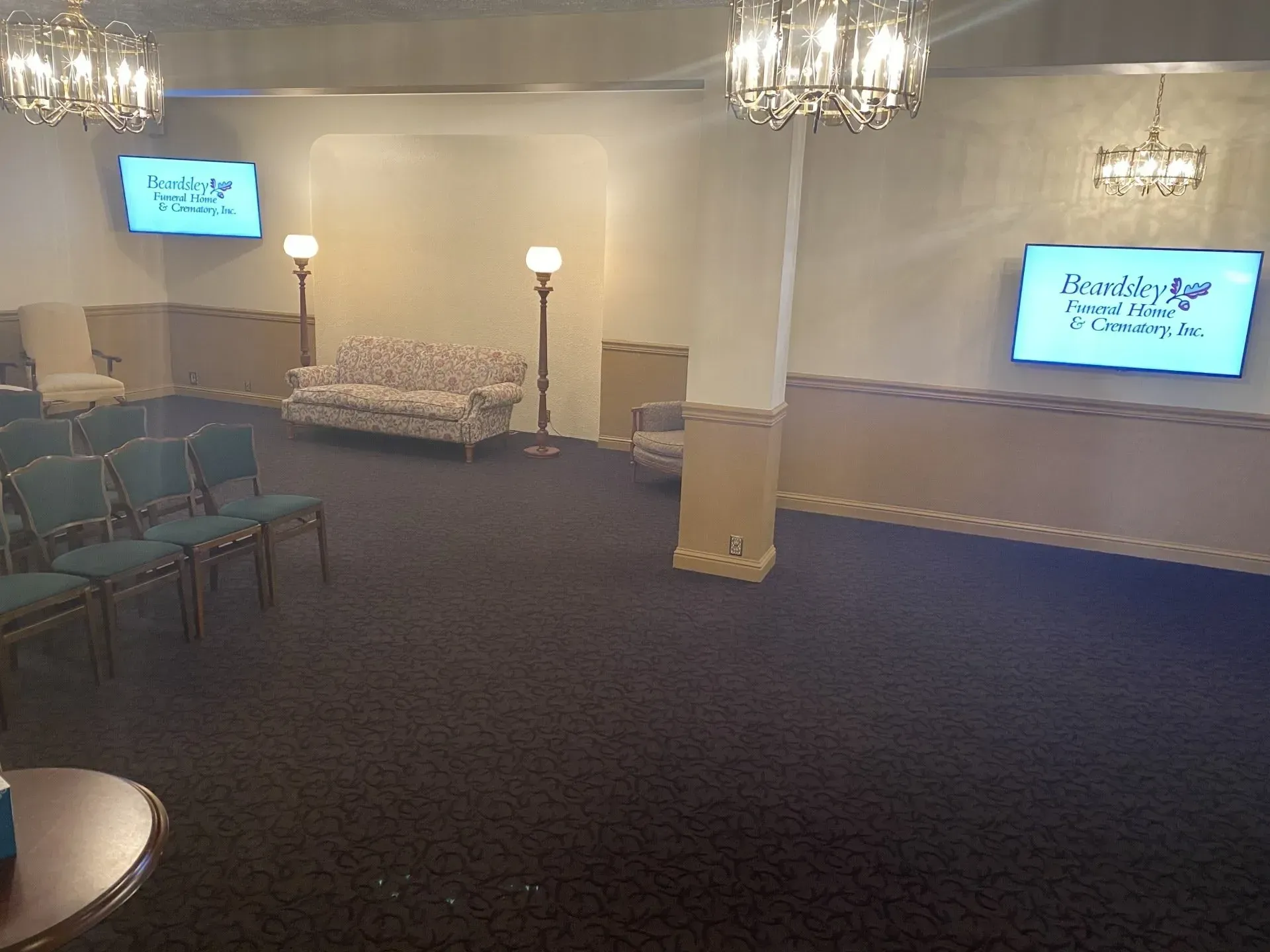 A large room with a couch and chairs and two televisions on the wall.