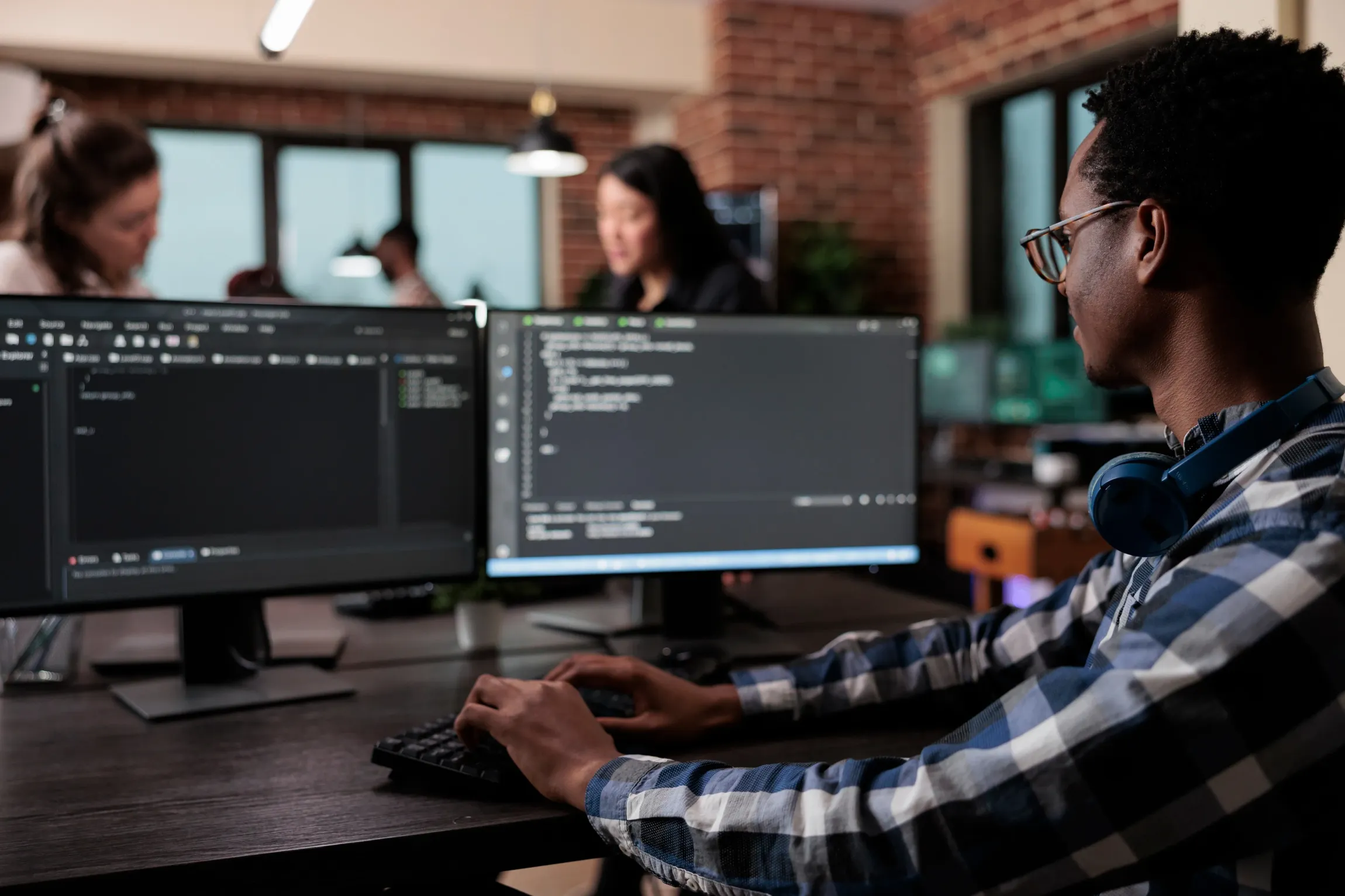 A man is sitting at a desk in front of two computer monitors.