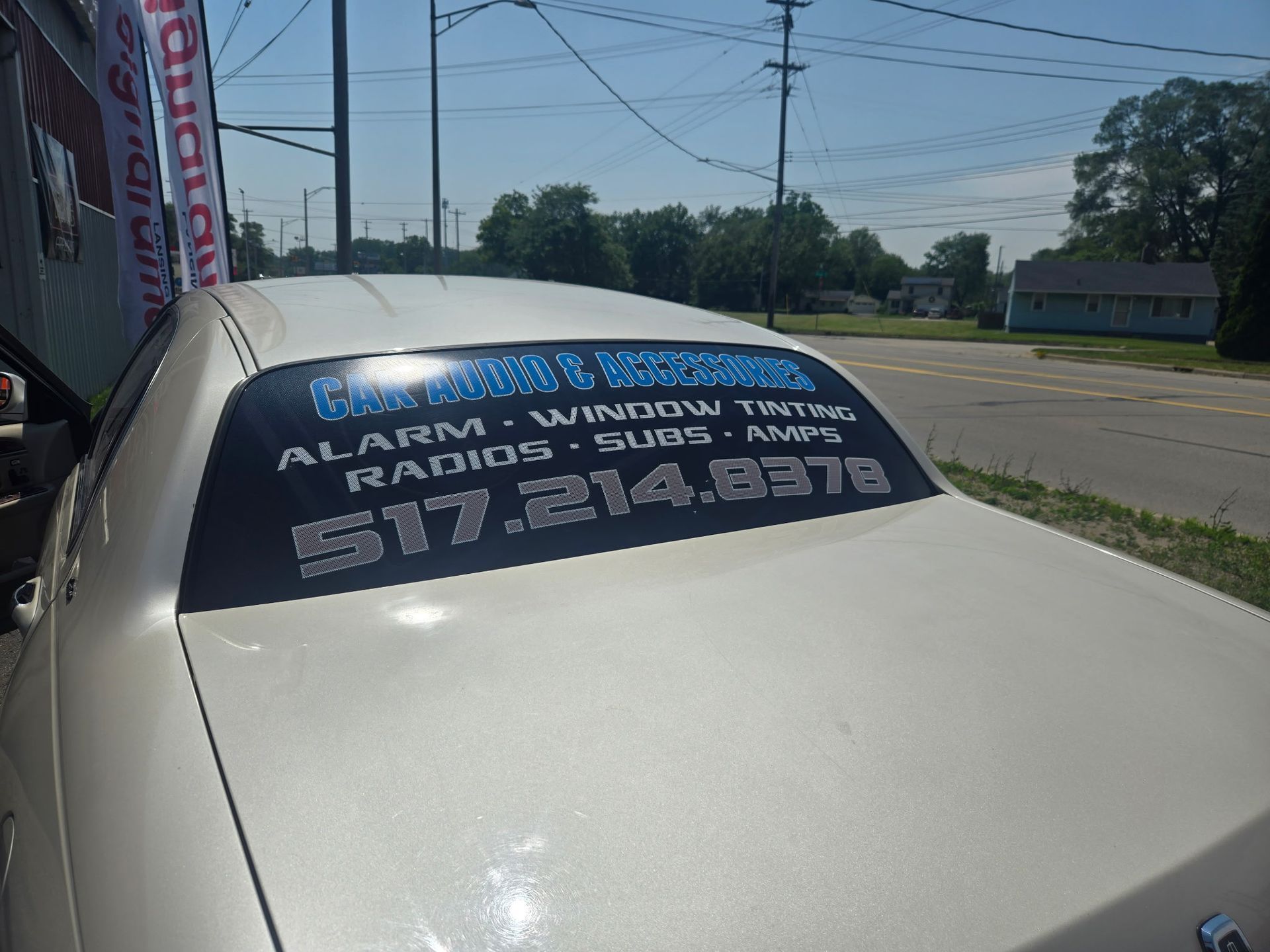 White car's rear window with business advertisement: alarm, tinting, radios, subs, and maps. 517.214.8378.