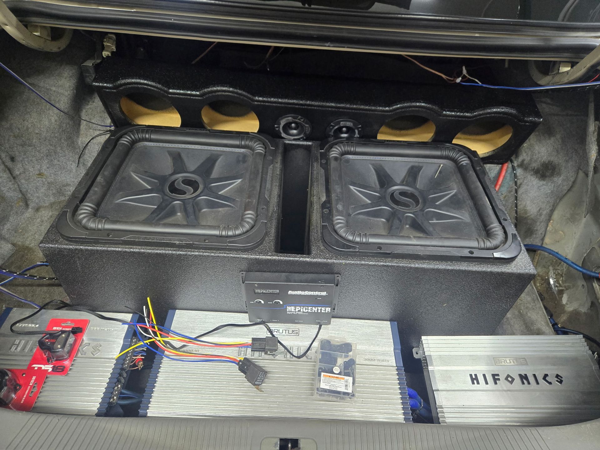 Car trunk with a large speaker box, two subwoofers, amplifiers, and wiring.