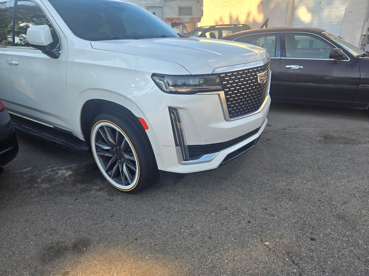 White Cadillac SUV with custom rims parked on asphalt.