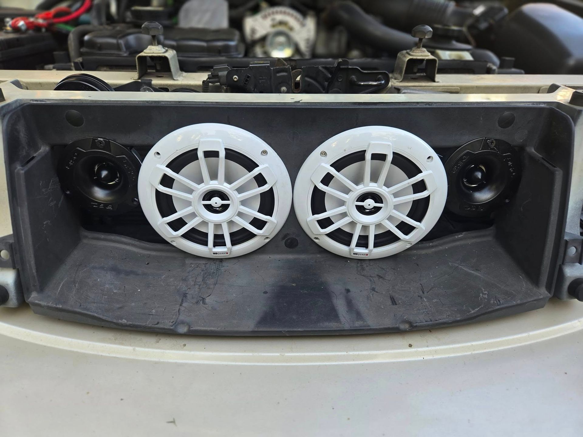 Two white circular speakers mounted in a car's dashboard, with two black speakers on the sides.
