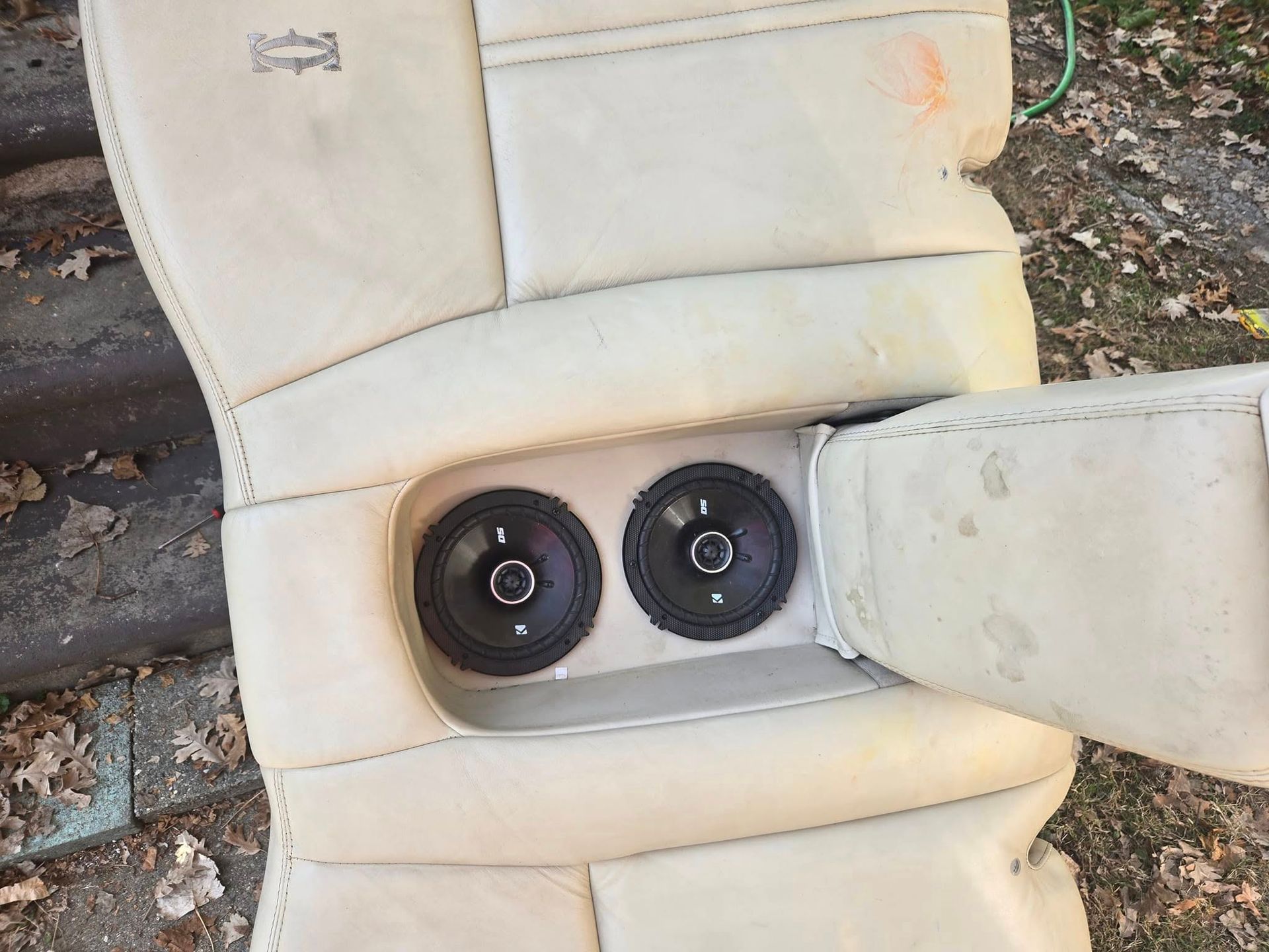 Two black car speakers installed in a light-colored car seat.