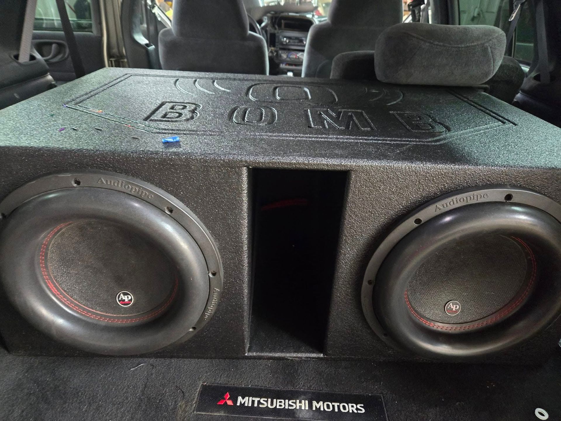 A black subwoofer box with two speakers installed in the back of a Mitsubishi SUV.