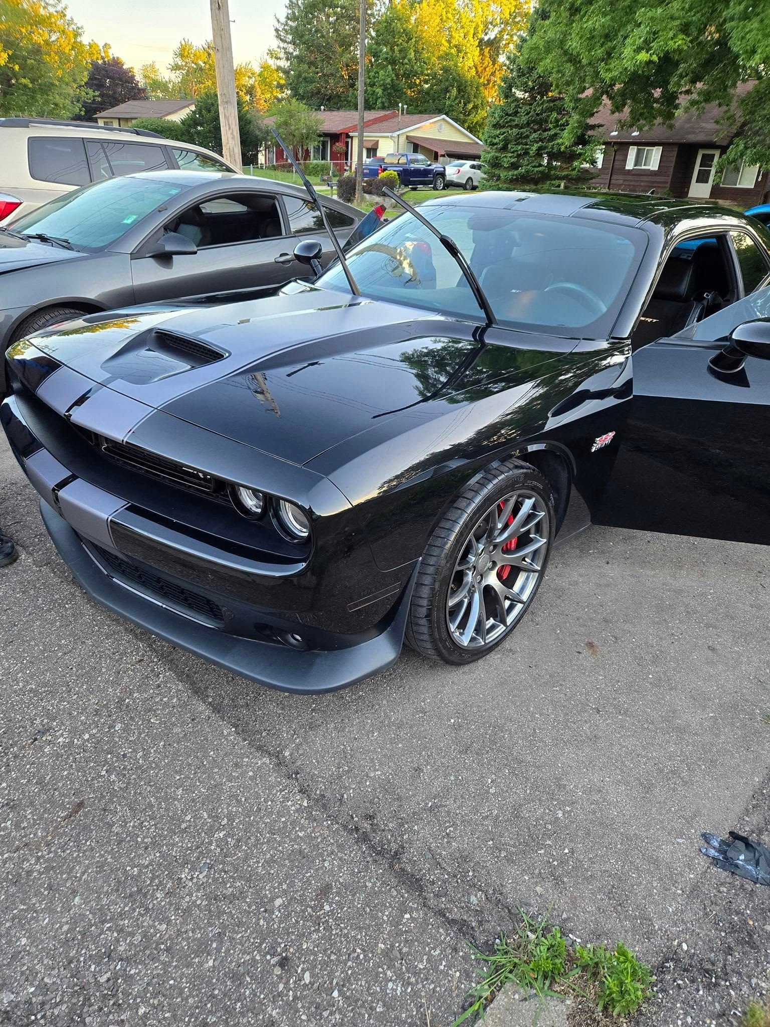 Black Dodge Challenger with racing stripes, parked on pavement, door open.