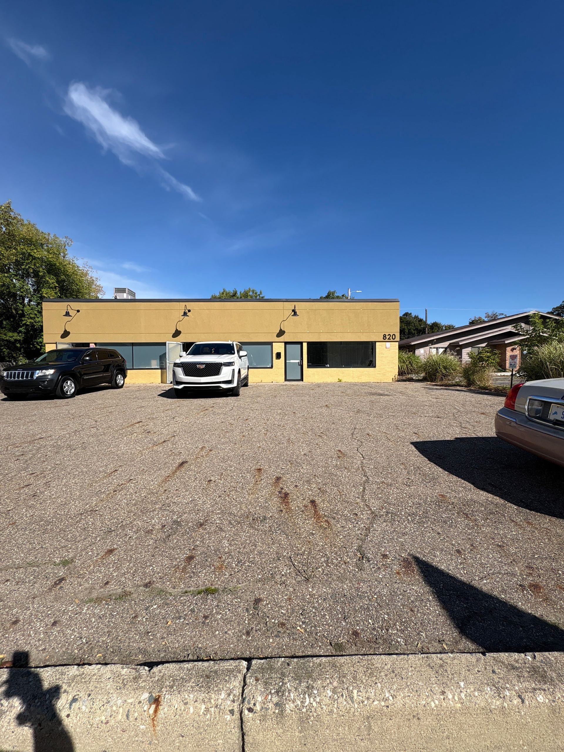 Yellow building with blue accents, gravel lot, and parked vehicles under a blue sky.