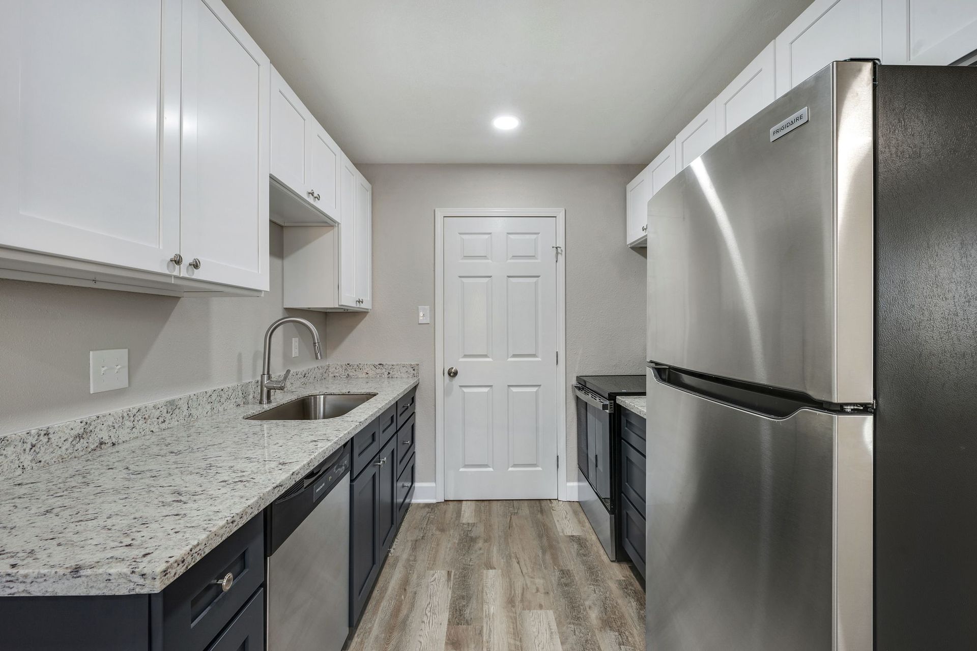 A modern kitchen features white upper cabinets, dark lower cabinets, granite countertops, and stainless steel appliances.