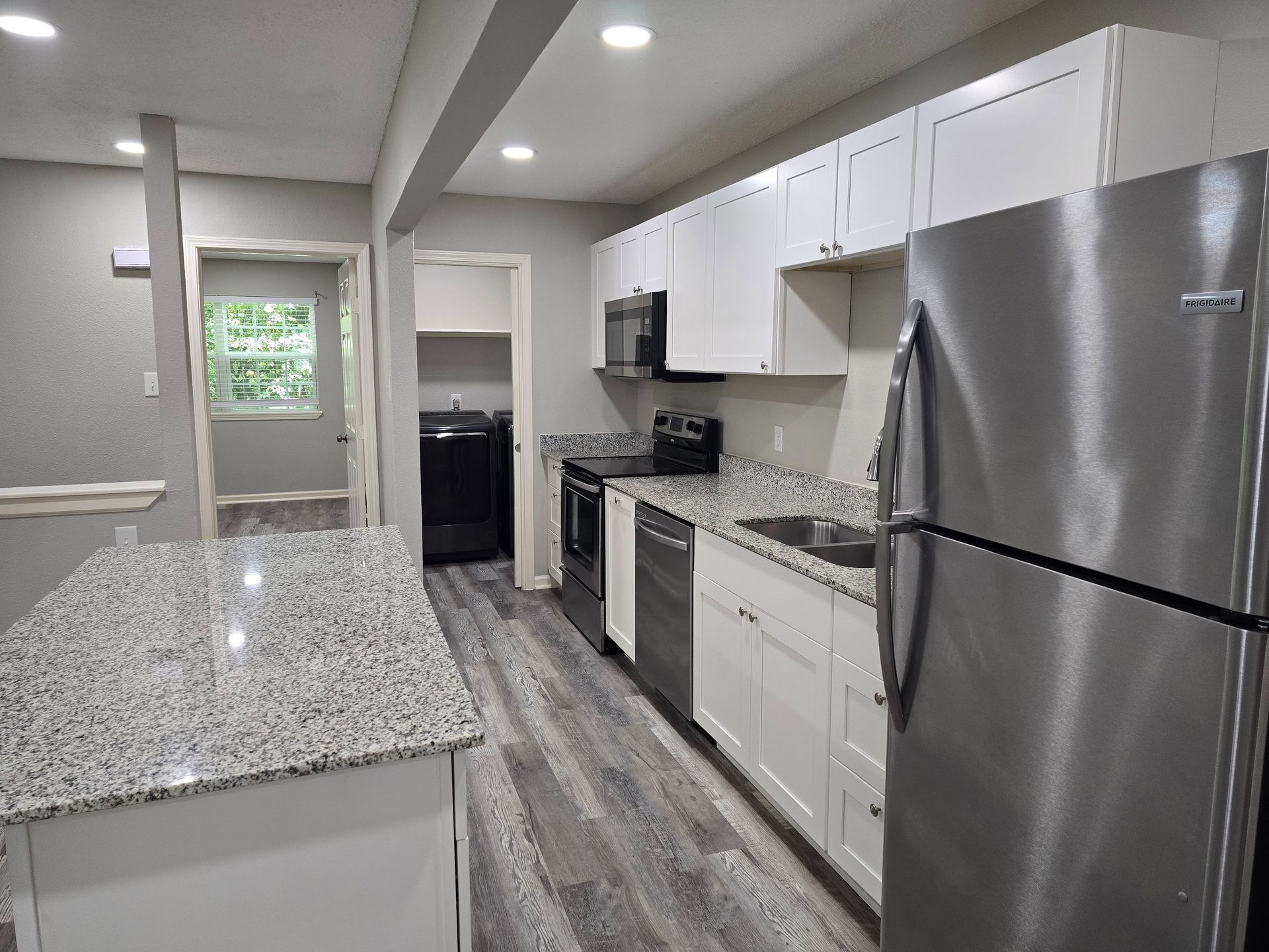 Modern kitchen with a gray granite island, stainless steel appliances, white cabinets, and wood-look laminate flooring.