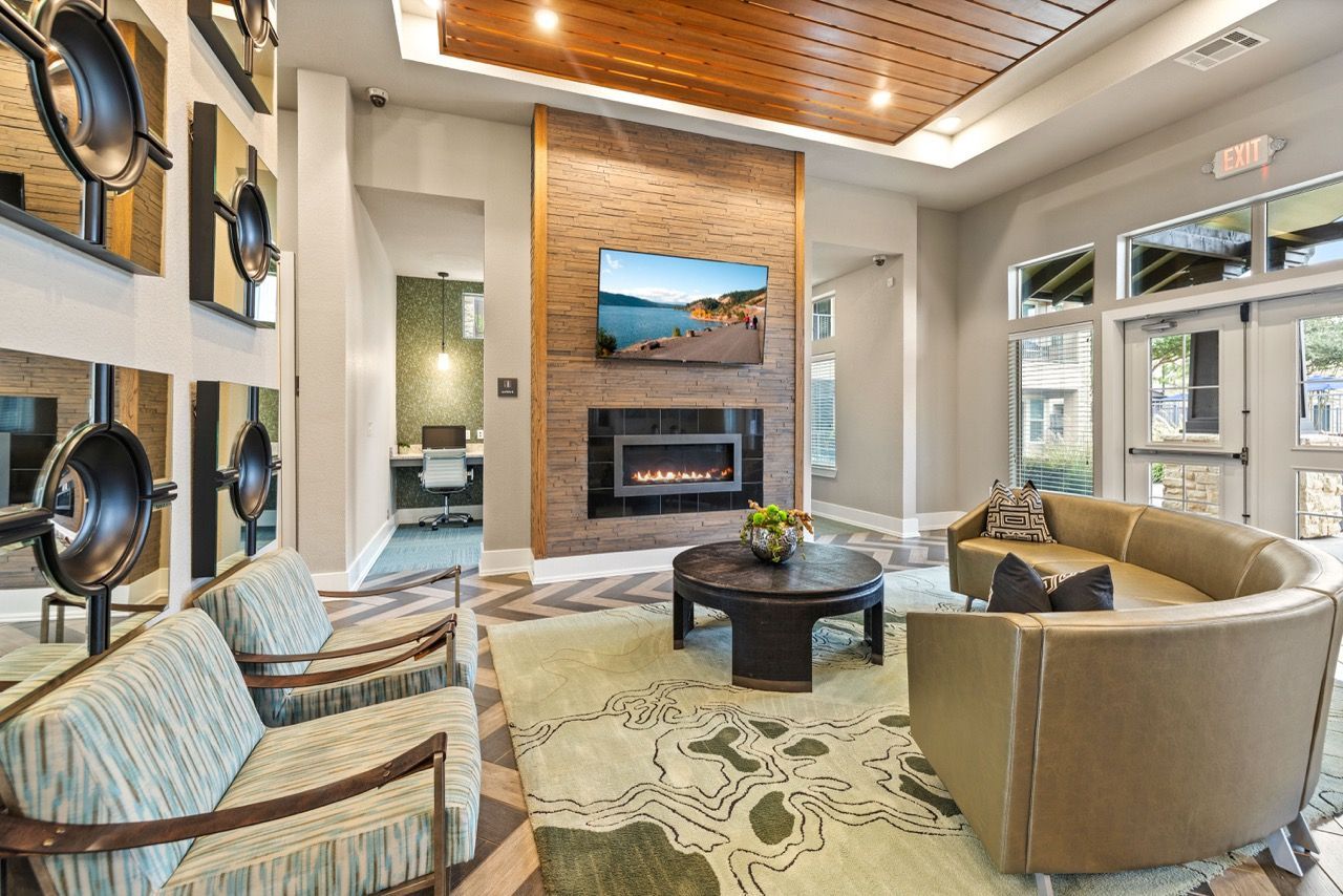 Contemporary community lounge with a stone fireplace, wall-mounted TV, round coffee table, and curved seating.