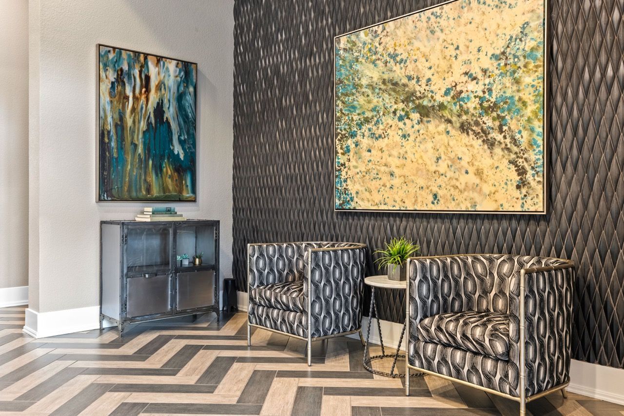 Lobby seating area with two patterned chairs, side table, and abstract wall art.