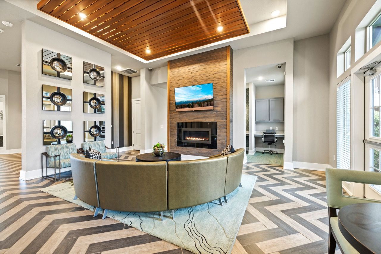 Contemporary apartment lobby with a stone fireplace, wall-mounted TV, and circular seating.