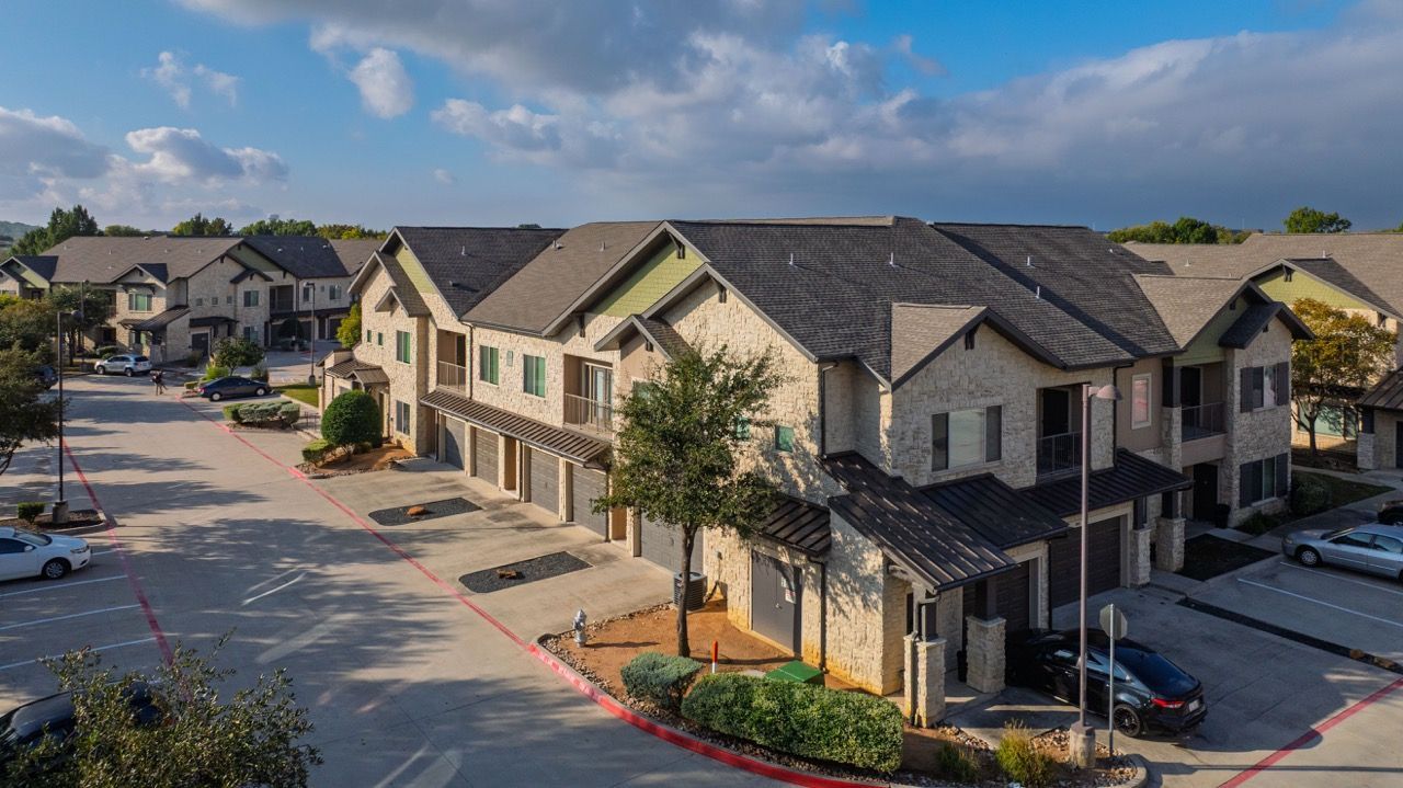 Aerial view of a multi-building apartment community with garages, trees, and parking.