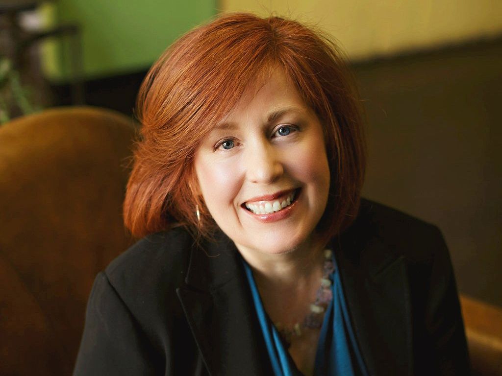 A woman with red hair is smiling for the camera while sitting in a chair.