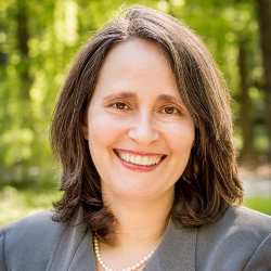 A woman in a suit and pearl necklace is smiling for the camera.
