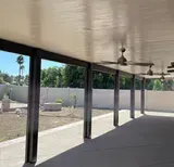 Covered patio with concrete floor, columns, and ceiling fans. Backyard with a wall and trees.