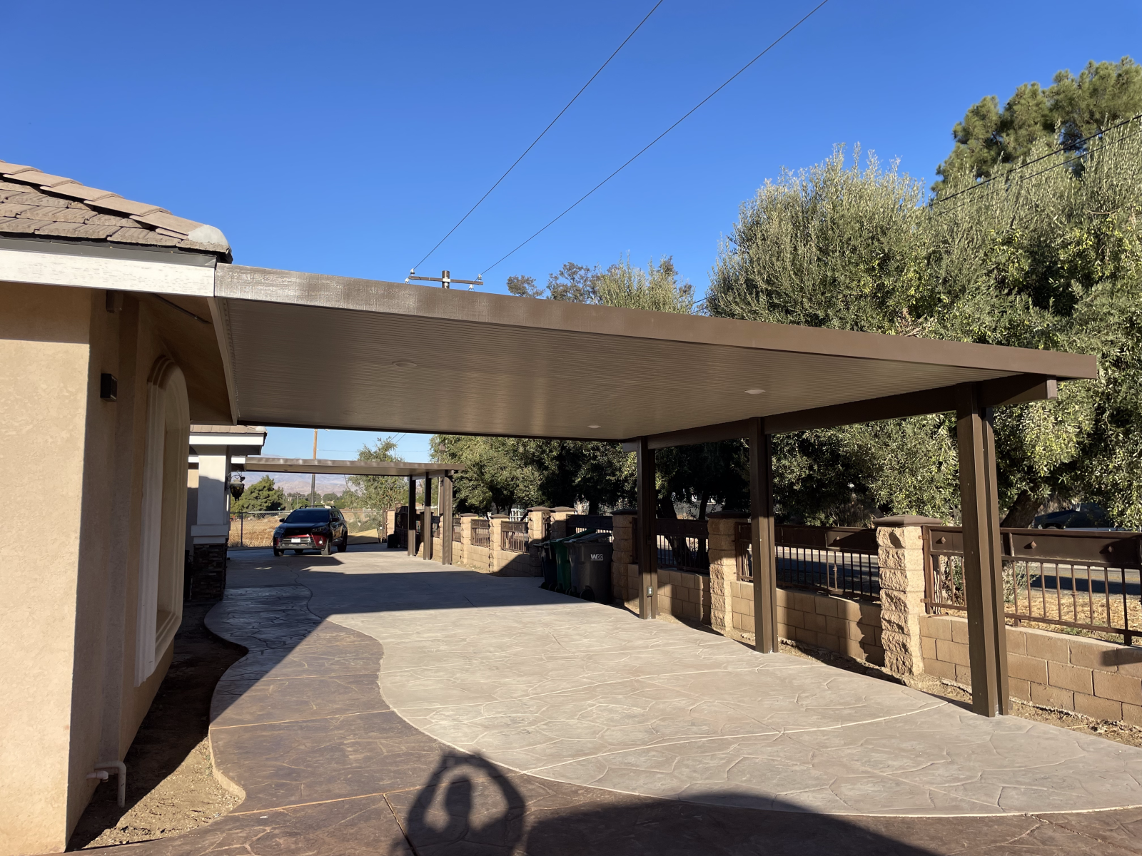 Carport attached to a house with a concrete driveway, under a clear blue sky.