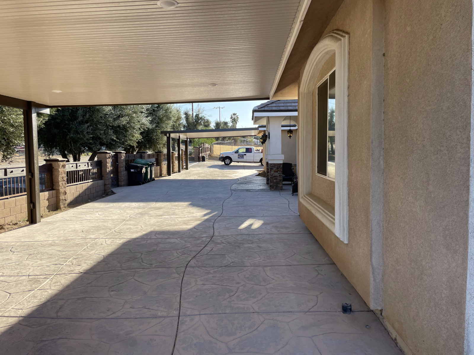 Long driveway next to a beige house, covered by a patio. A white truck is at the end of the driveway.