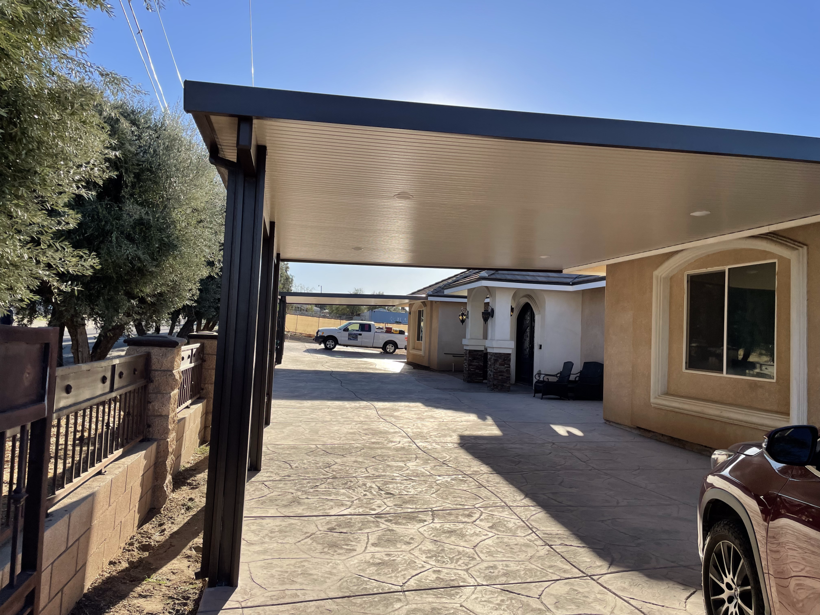 Driveway with a carport, tan house, and a pickup truck. Sunny day.