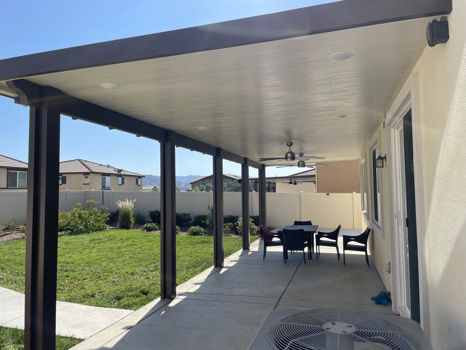 Patio with a covered seating area, chairs, and a ceiling fan. A backyard with a lawn and fence is visible.