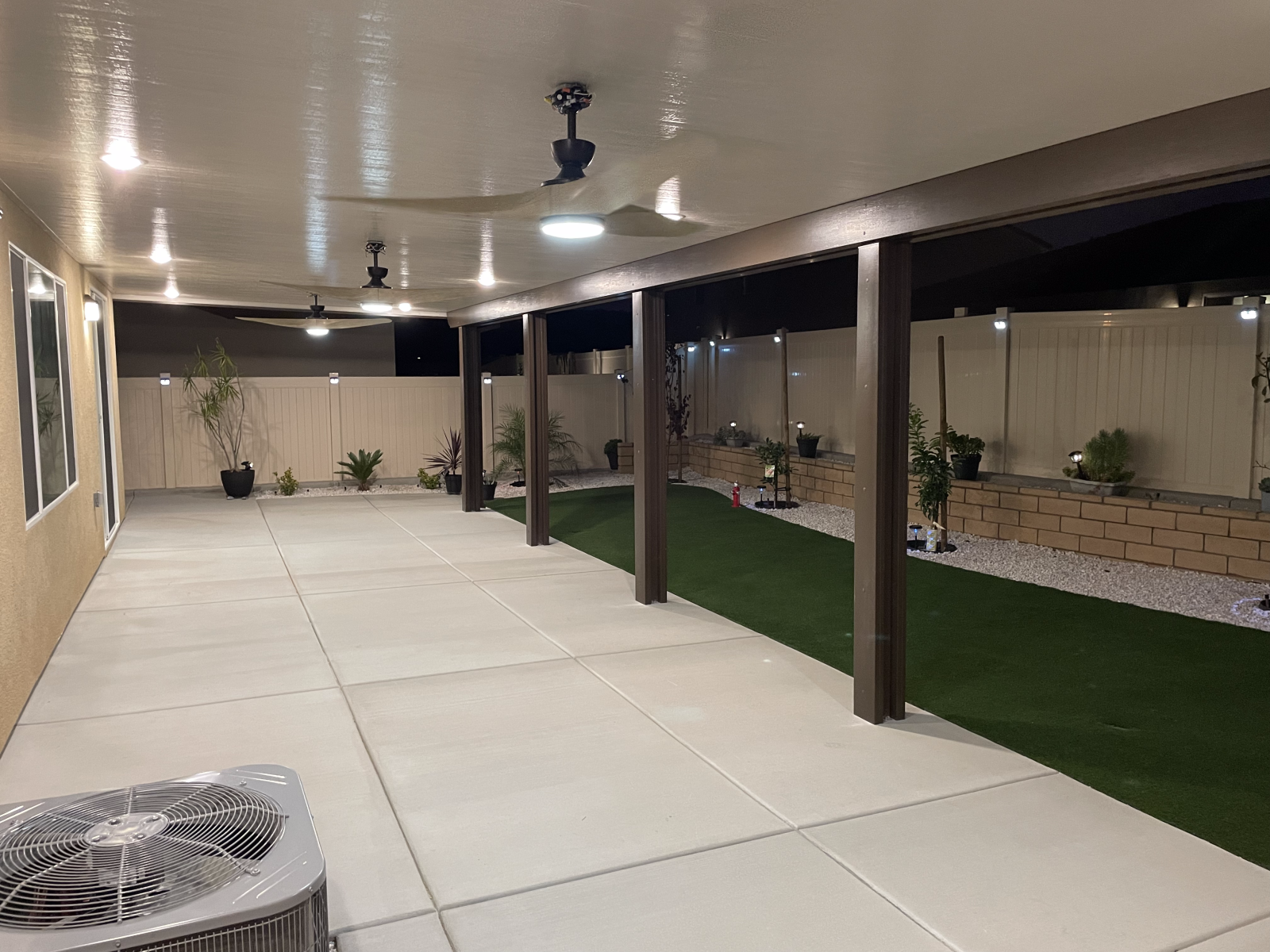 Covered patio with ceiling fans, lights, concrete flooring, and artificial grass.