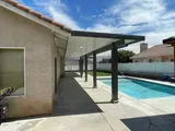 Patio with dark gray canopy over concrete, next to a pool.
