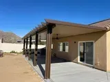 Brown patio cover attached to a beige house, with a concrete patio.