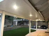 Patio with white ceiling, recessed lights, and view of a backyard with green grass, fence, and seating area.