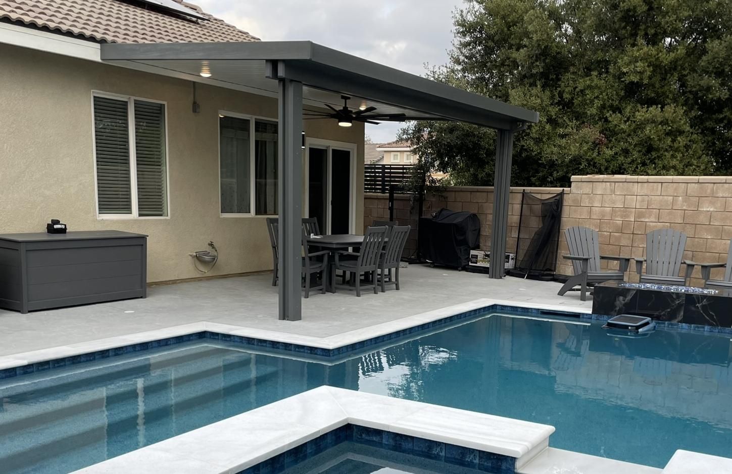 Patio with pool, gray pergola, outdoor dining set. Neutral color scheme, clear blue pool water.