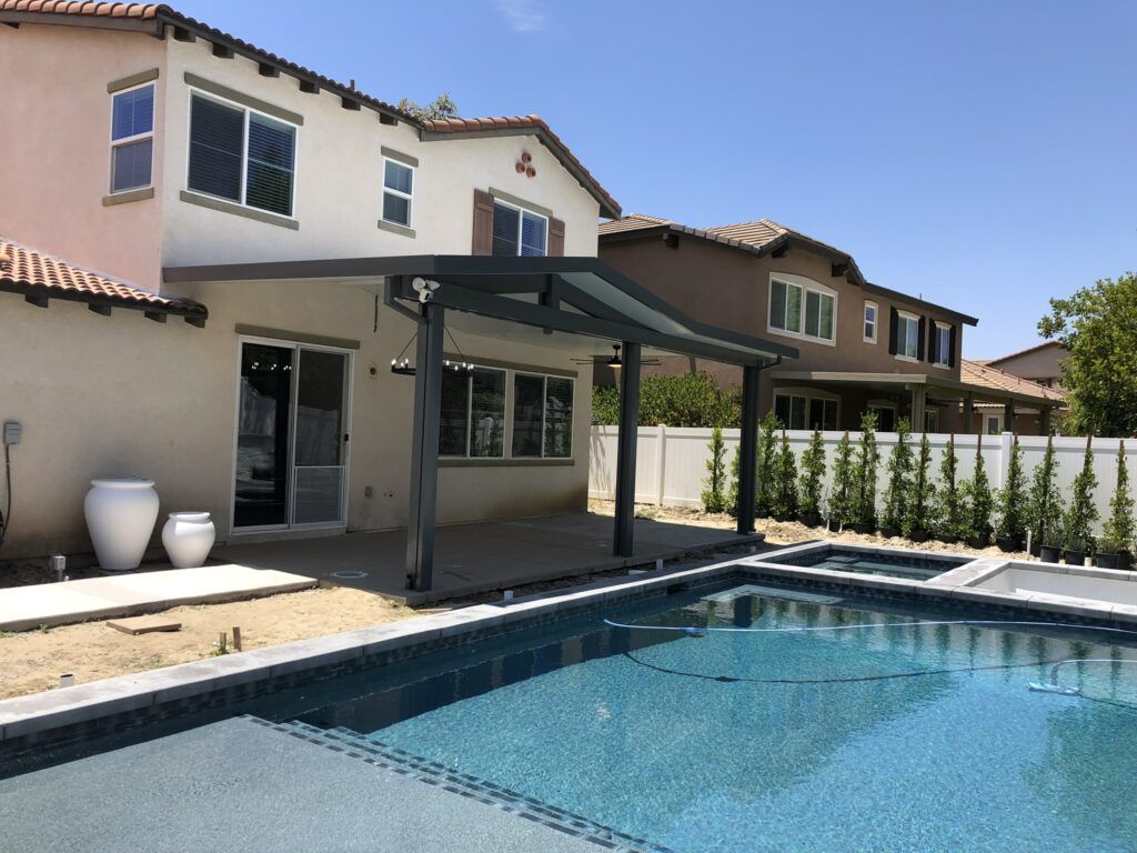 Backyard with a pool, patio, and two-story house. White fence and plants line the yard.
