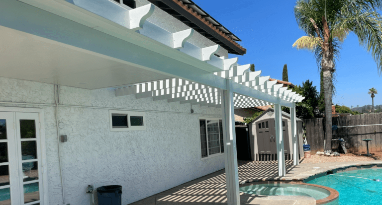 White pergola and patio next to a swimming pool, sunny day.
