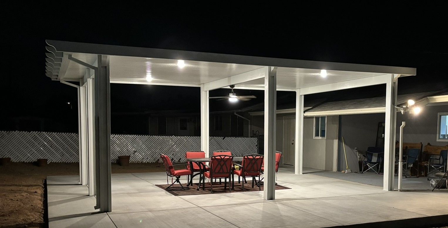 Patio with red chairs and table under a white canopy with lights at night.